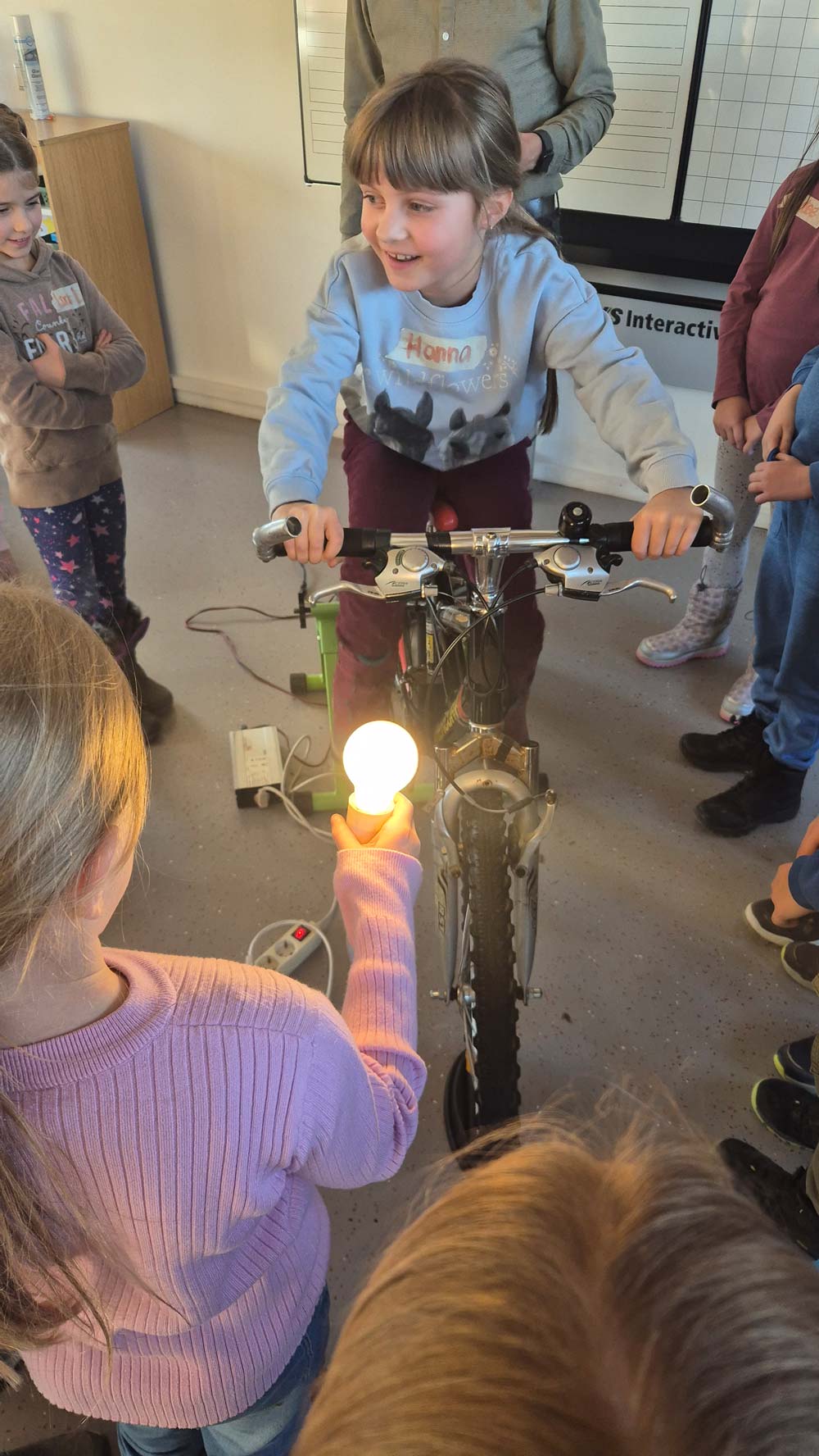 Kind produziert auf Fahrrad Strom für eine Glühbirne